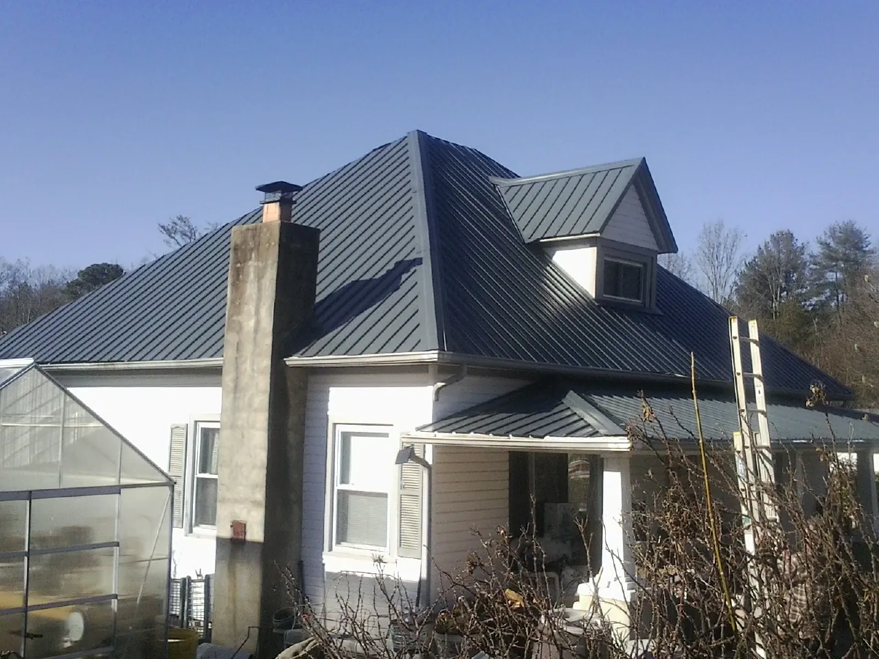 Dark blue standing seam metal roof on a white farmhouse with dormer — Slate & Tile Roof Repair by Roofing Brothers in Piney Flats