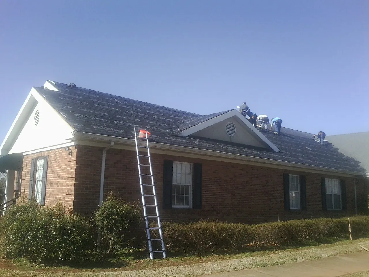 Crew tearing shingles off a brick ranch roof with a ladder set — Emergency Roof Repair work by our crew in Piney Flats