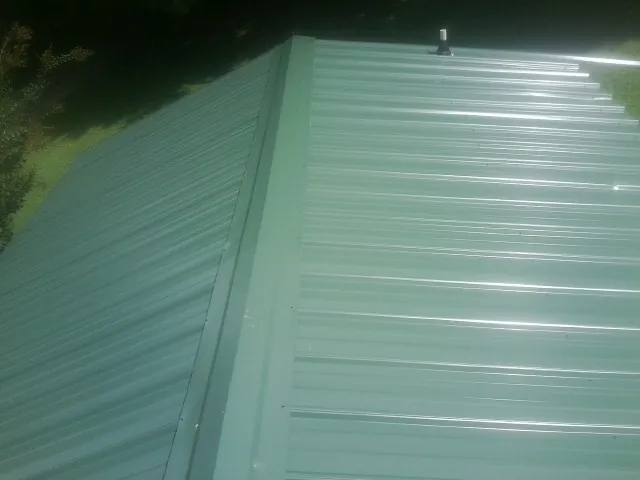 New green metal panels meeting at the ridge of a roof — Flat Roof Repair work by our crew in Piney Flats