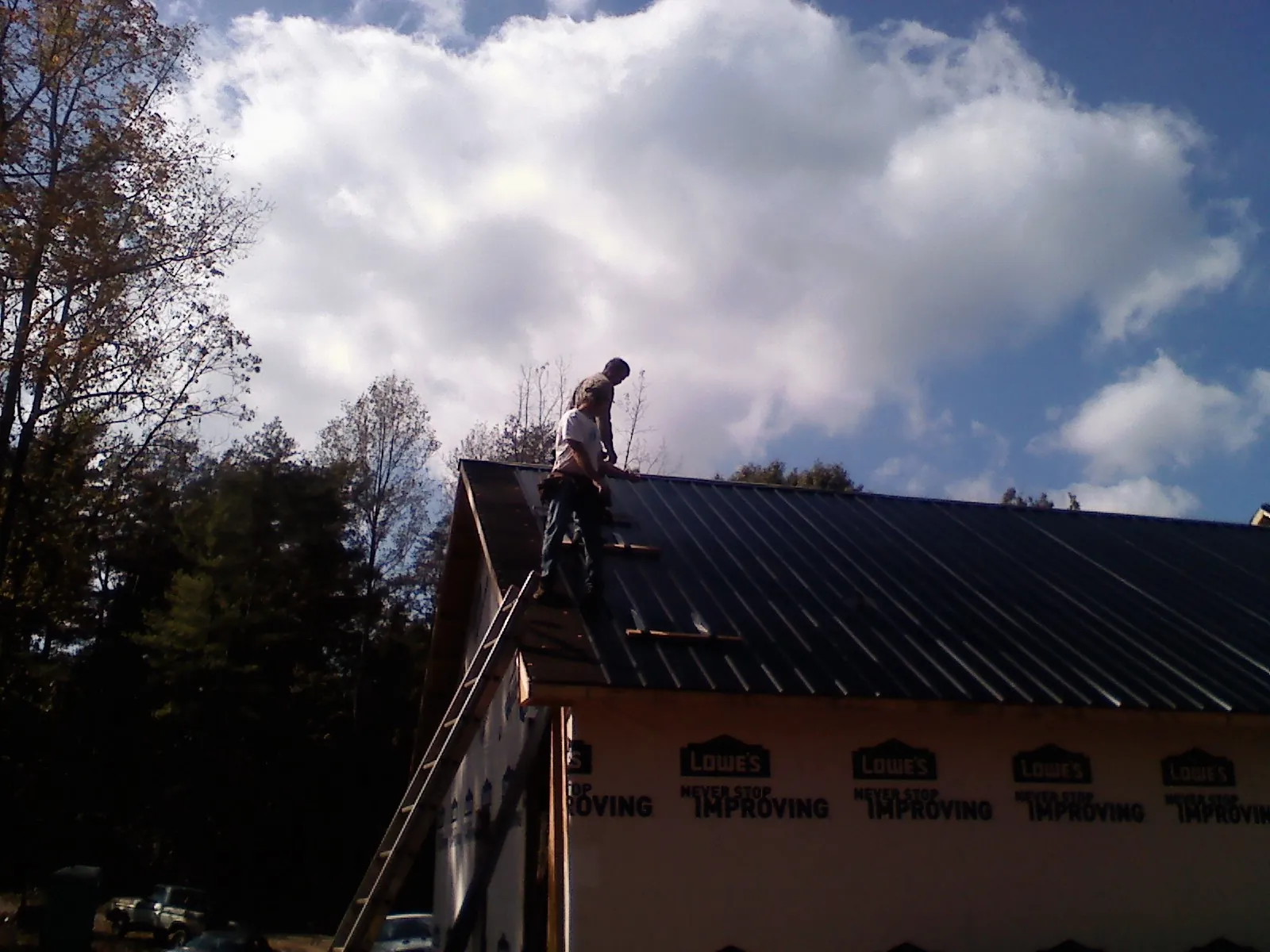 Roofer fastening dark metal panels high against a cloudy sky, from a Roof Inspection job in Piney Flats