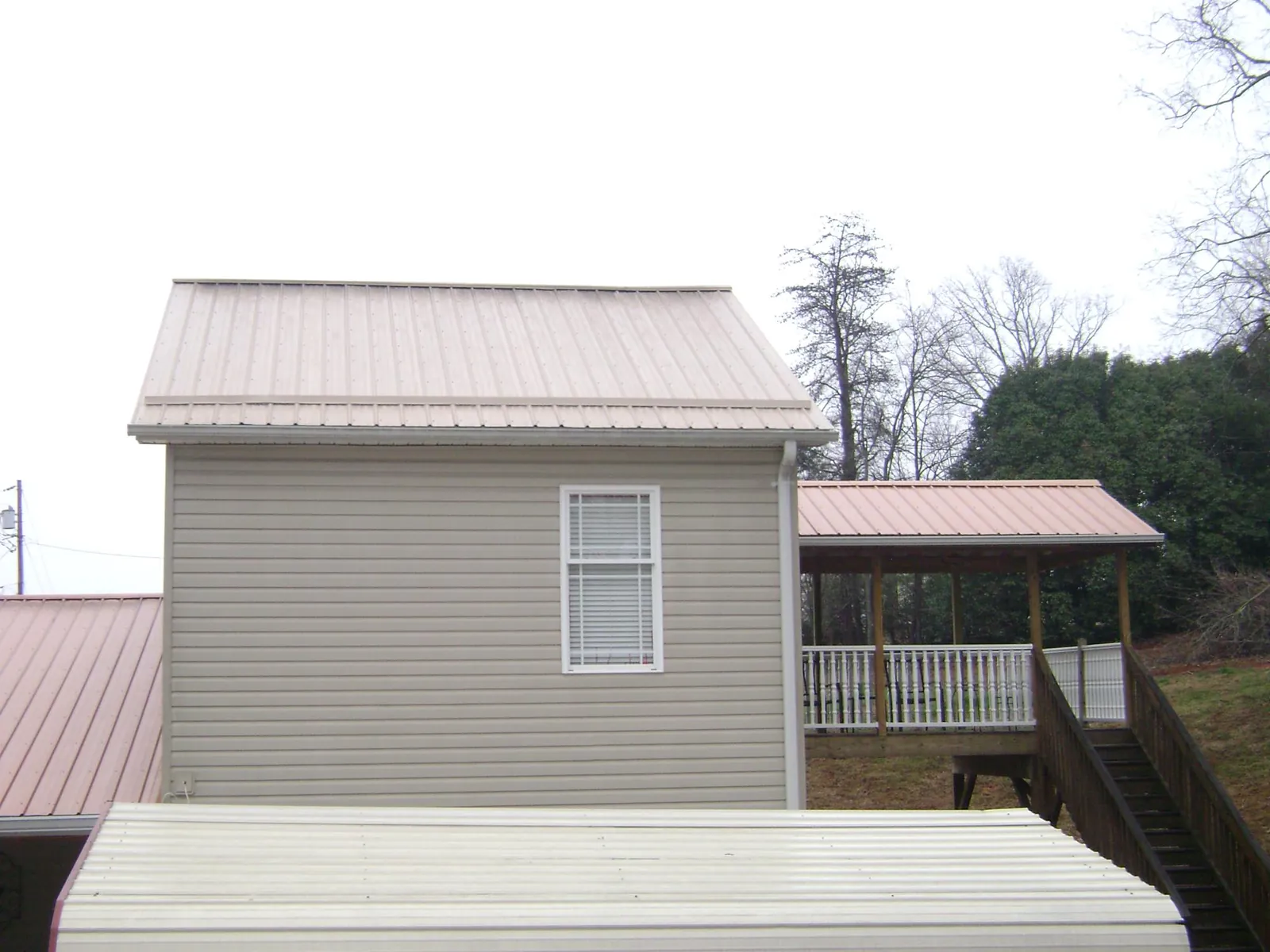 Tan metal roofs on a two story addition and attached porch, from a Roof Replacement job in Piney Flats